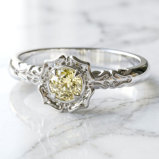 A lab created light yellow sapphire centerpiece engagement ring with a stylized flower petal setting, made of white gold.