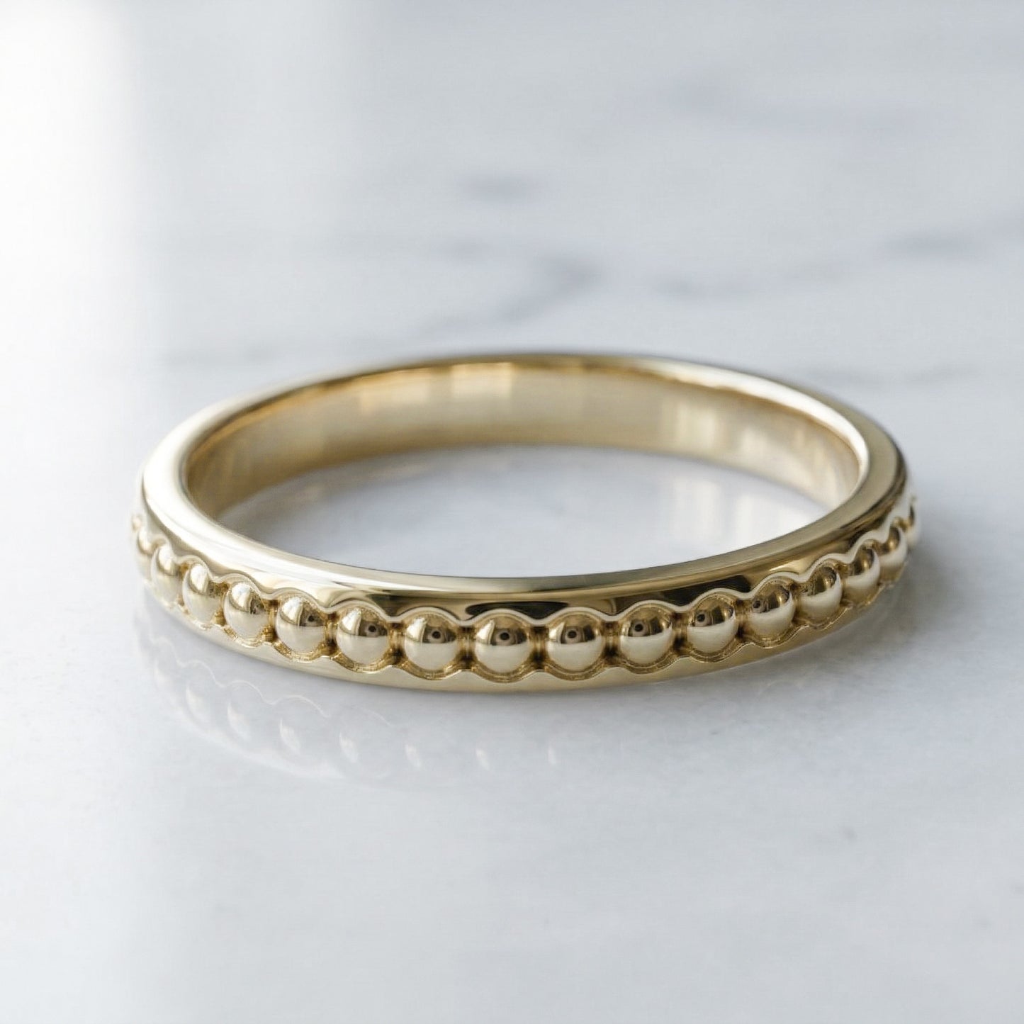 yellow gold ring with beaded design on a light gray background