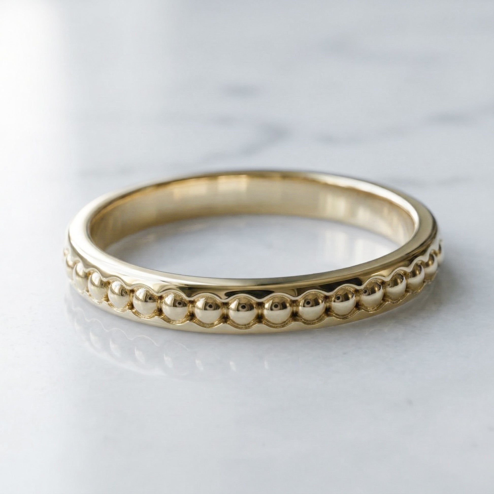 yellow gold ring with beaded design on a light gray background