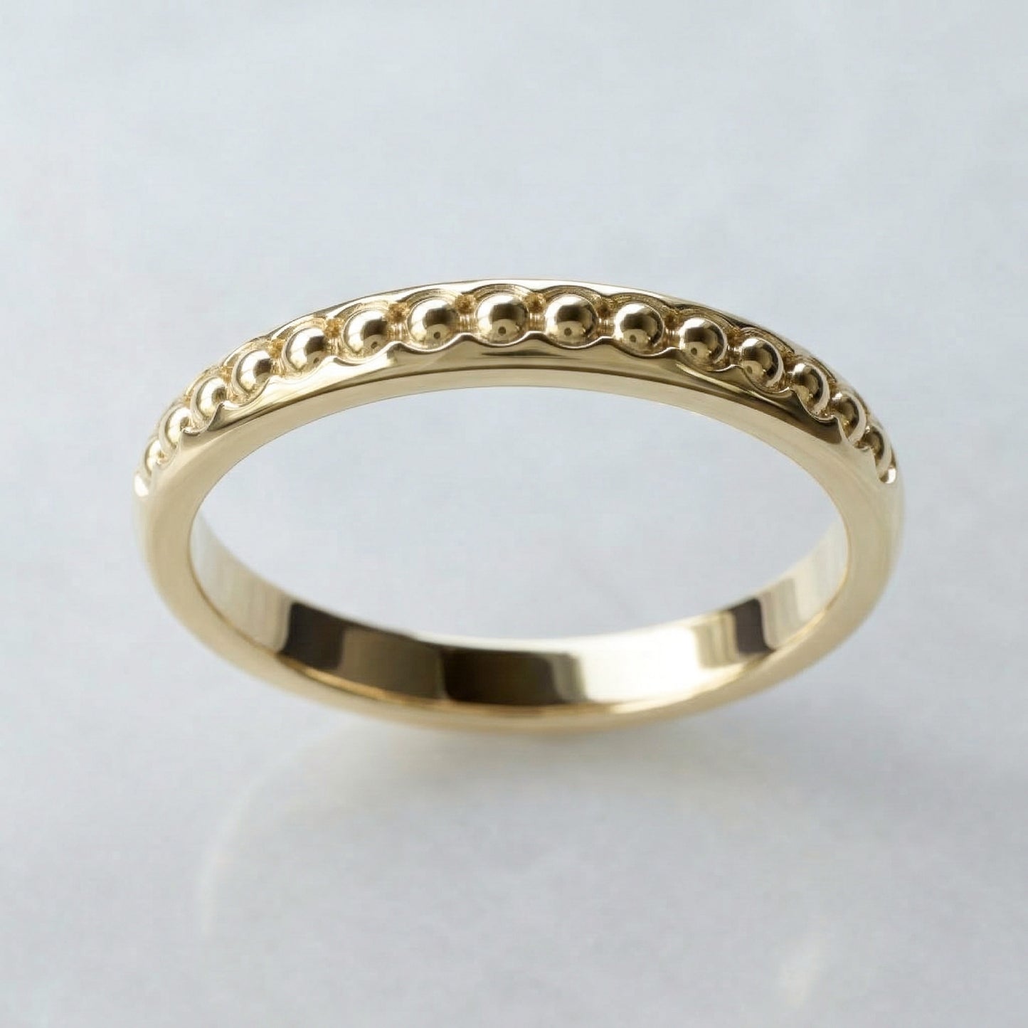 Gold ring with balls band on a light gray background