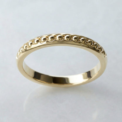 Gold ring with balls band on a light gray background