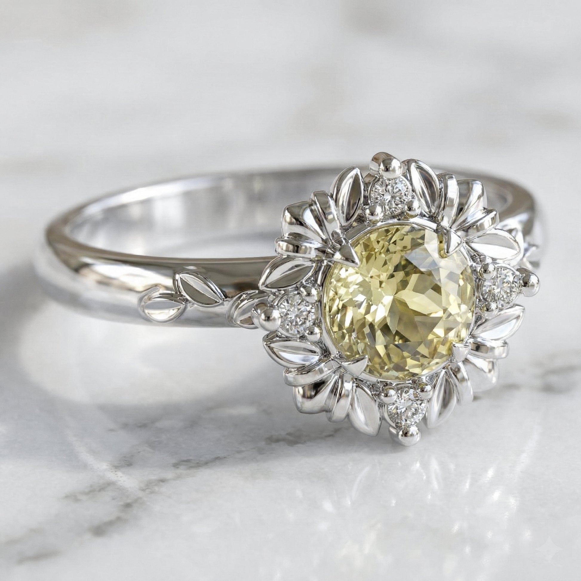 White gold ring with a light yellow sapphire on a marble surface