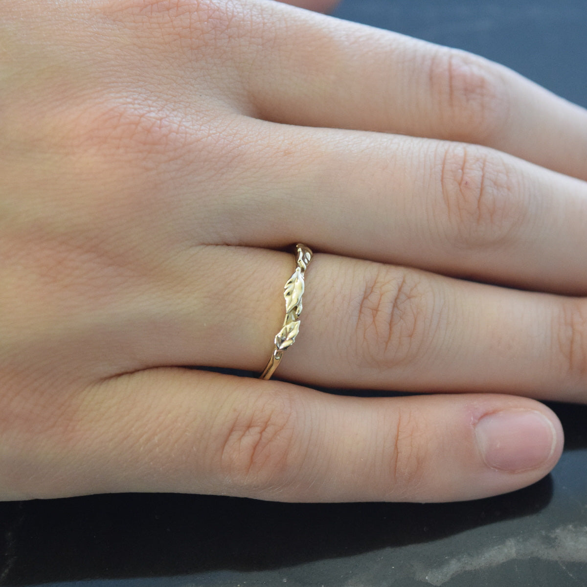 yellow gold wedding band with leaves on finger
