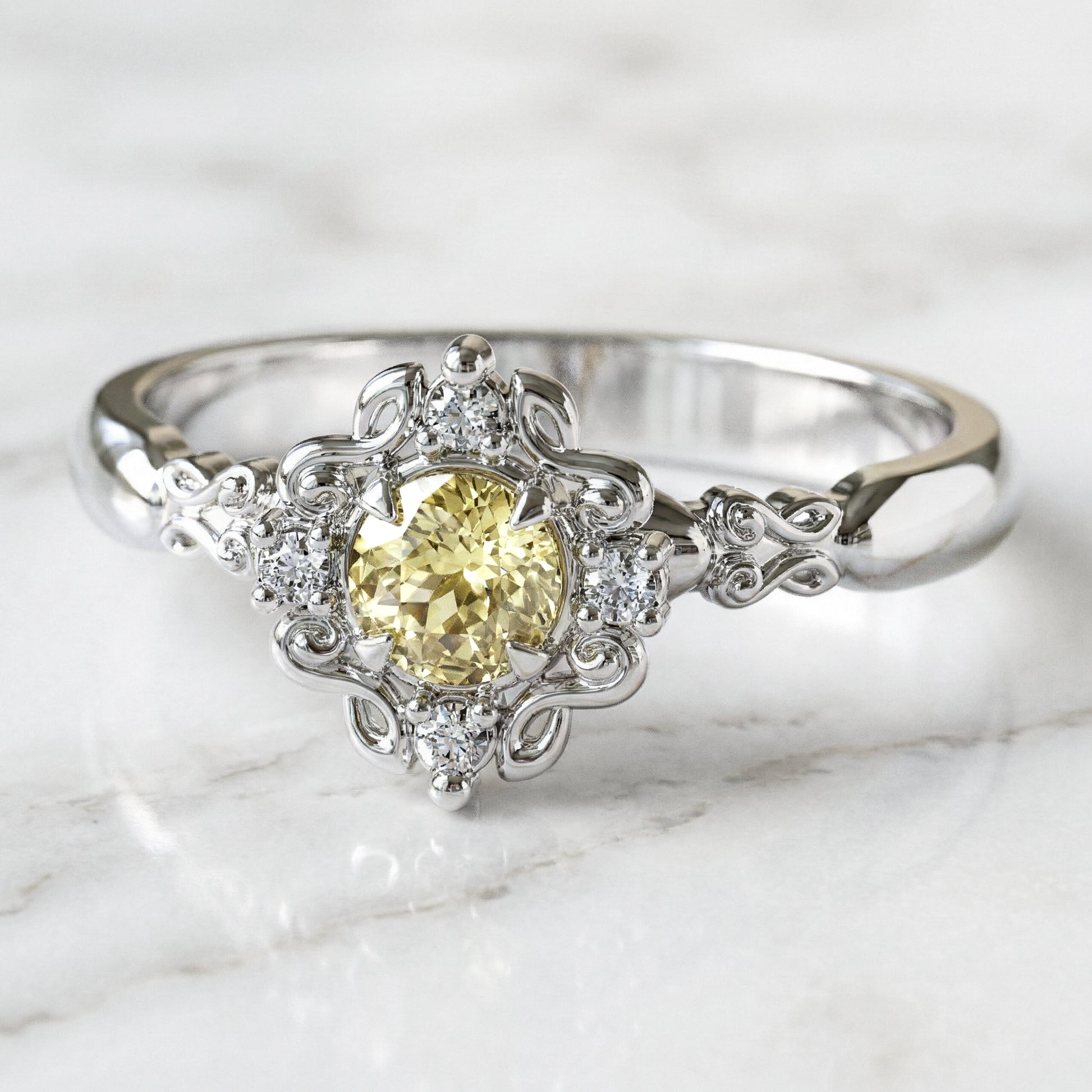 A round engagement ring with a central light yellow sapphire, flanked by four small lab-grown diamonds, set in a gold filigree setting.