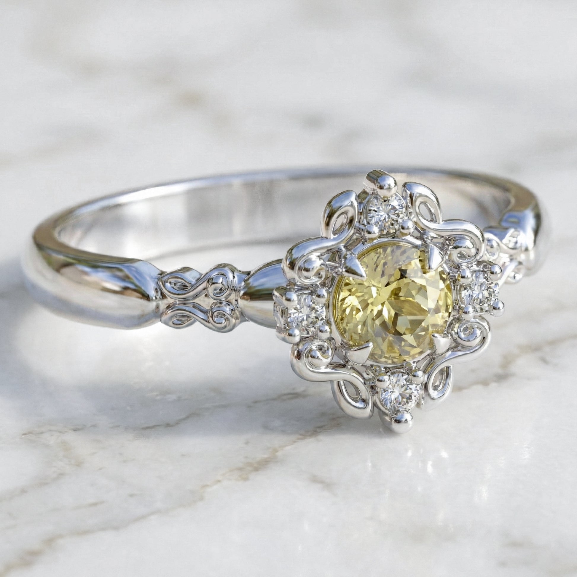 A round engagement ring with a central light yellow sapphire, flanked by four small lab-grown diamonds, set in a gold filigree setting.
