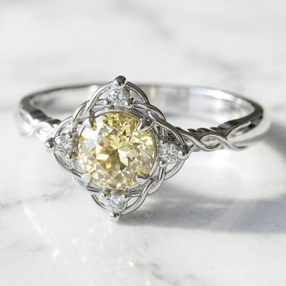 A round engagement ring with a central lab-created light yellow sapphire gemstone, flanked by four small lab-created diamonds, all set in a white gold band.